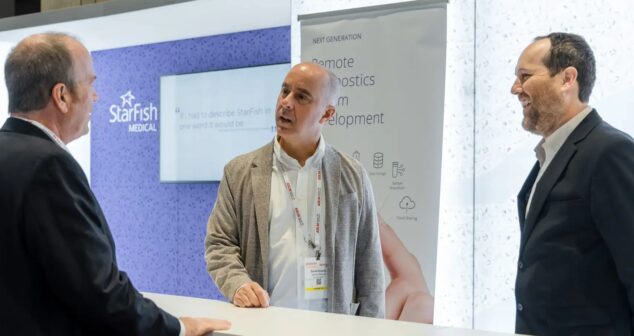 Three professionals talk at a StarFish Medical trade show booth, with signage highlighting remote diagnostics and medical device development in the background.