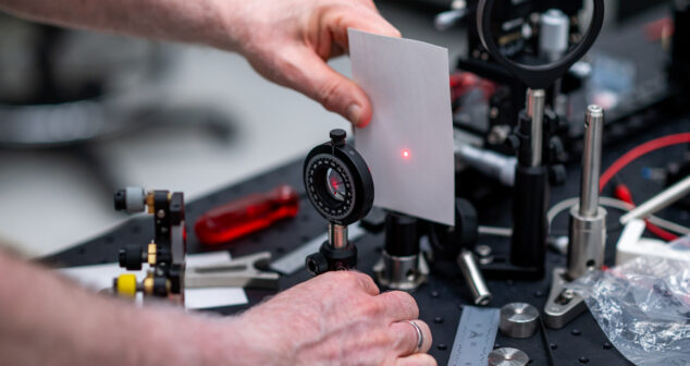 Engineer aligning a red laser beam through optical components in a lab setup