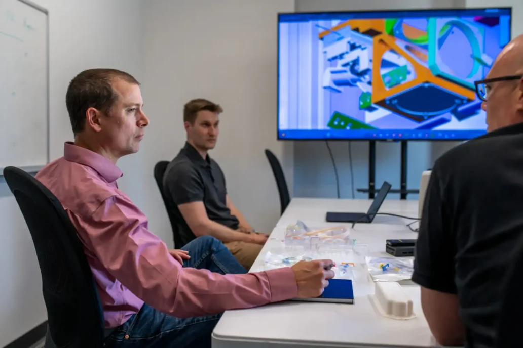 Medical device engineers in a design review meeting discussing 3D CAD models on screen with prototypes and components on the table at StarFish Medical.