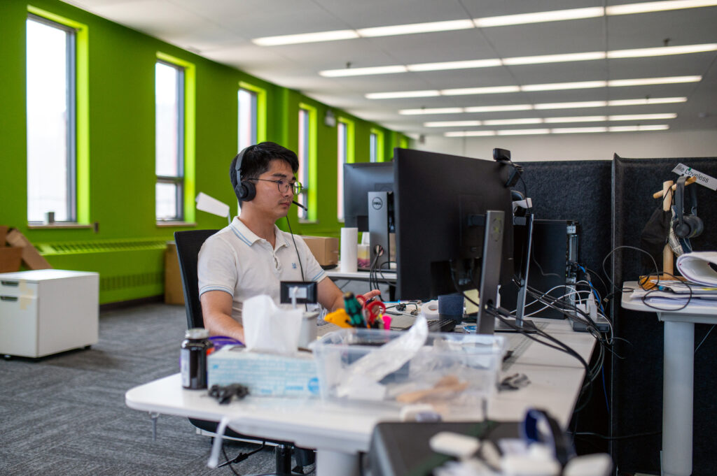 Medical device engineer wearing a headset and working at a computer in an open office with green walls.