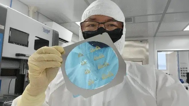 Engineer in cleanroom PPE holding a wafer with microfluidic device patterns during medical device fabrication