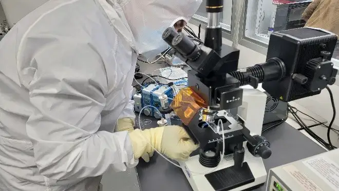 Technician in cleanroom using microscope for quality inspection of microfluidic device components