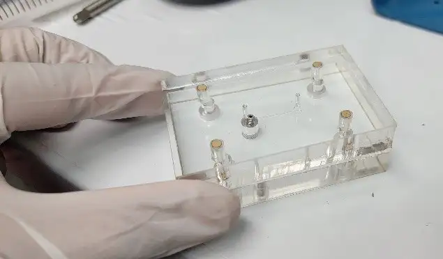 Gloved hands assembling a transparent microfluidic device cartridge with integrated ports and fastening components