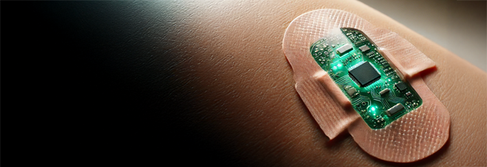 A close-up of a person's skin with a smart bandage applied. The bandage contains an embedded green-glowing electronic circuit, resembling a microchip, suggesting advanced medical monitoring or theranostic technology.